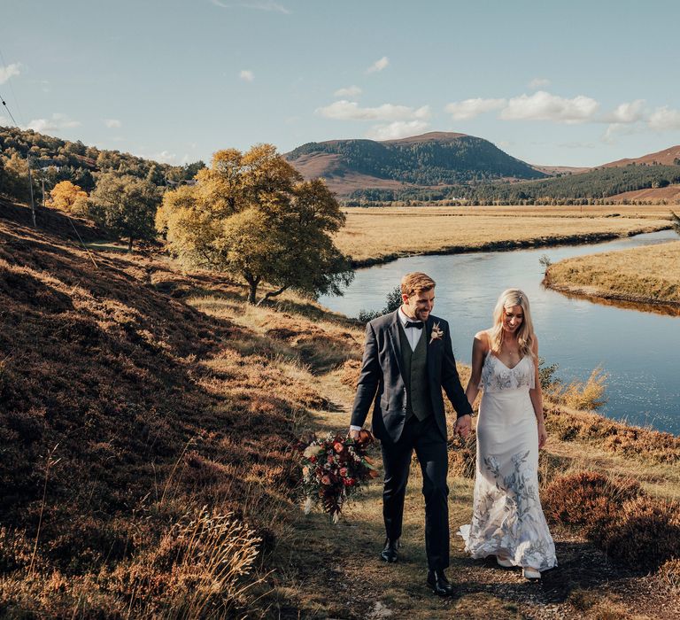 Bride & groom walk through Scottish countryside with lake in the background