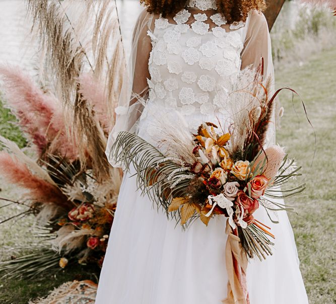 Bride stands in front of extravagant dried floral arrangement outdoors