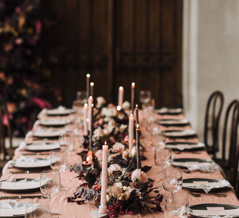 Intimate wedding reception table decor with blush pink and burgundy wedding flowers, taper candles and linens. 