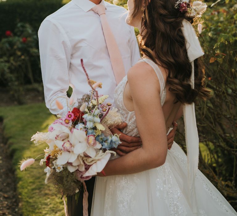 Bride & groom laugh together on the day of their wedding whilst the sun sets behind them