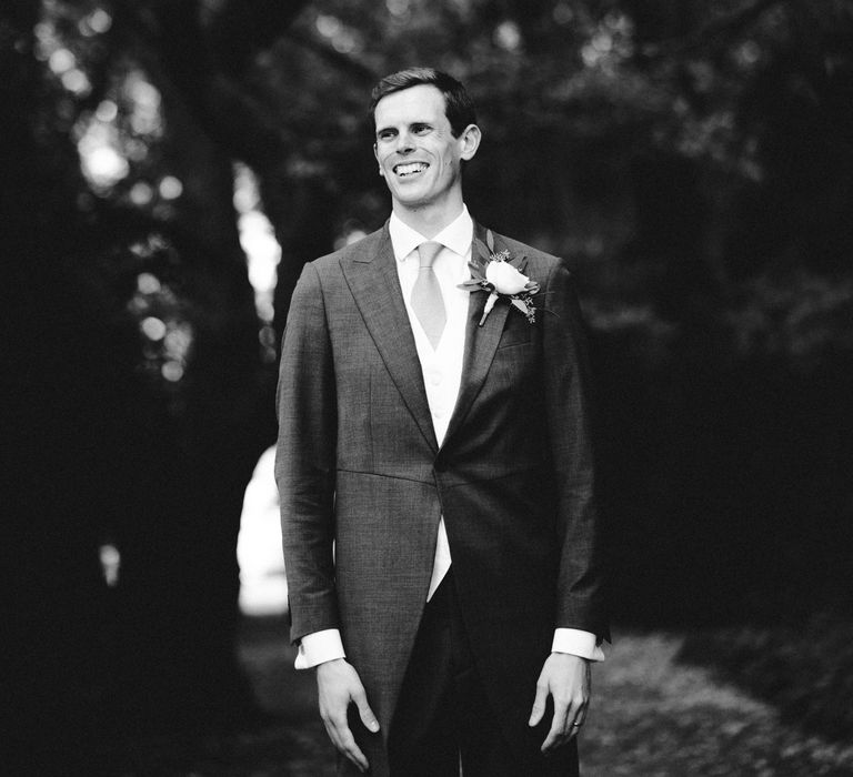 Black & white image of groom smiling outdoors 