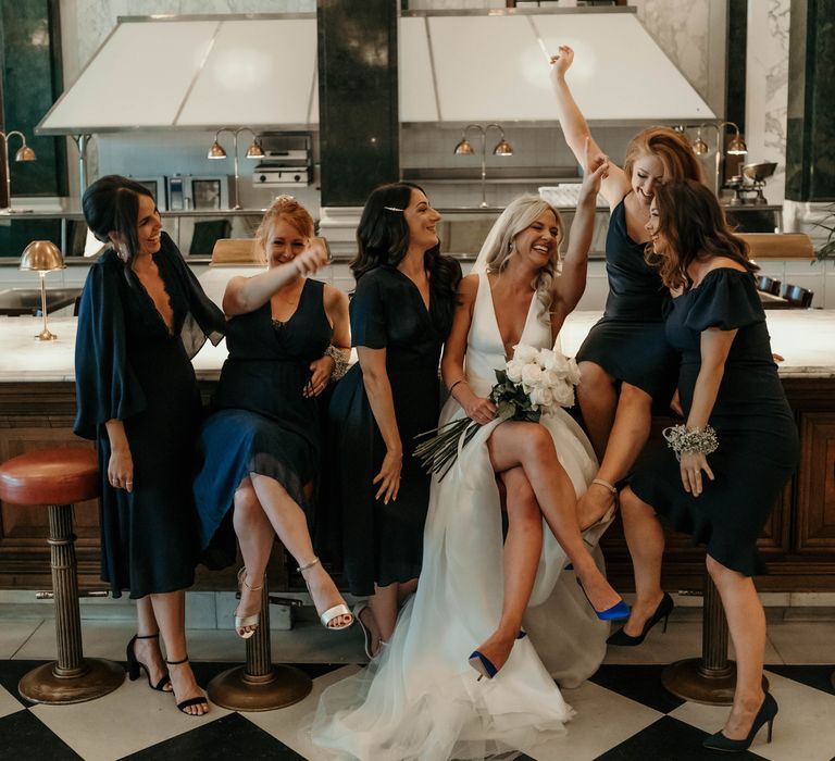 Bride laughs with bridesmaids in navy dresses on the morning of her wedding