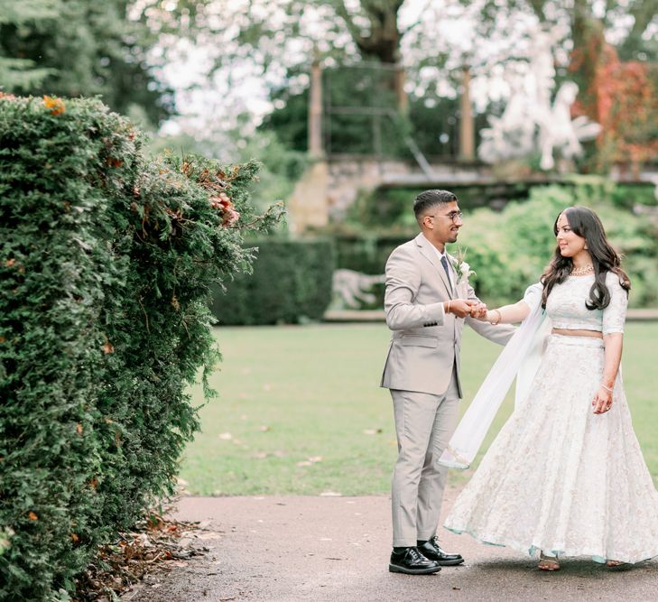 Groom in a beige suit twilling his bride in a mint green and white embroidered sari