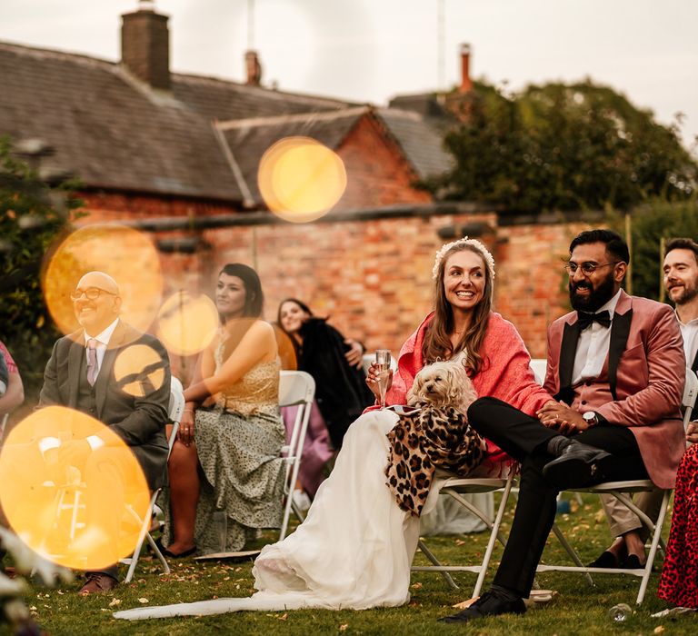 Bride & groom sit with wedding party outdoors whilst listening to speeches