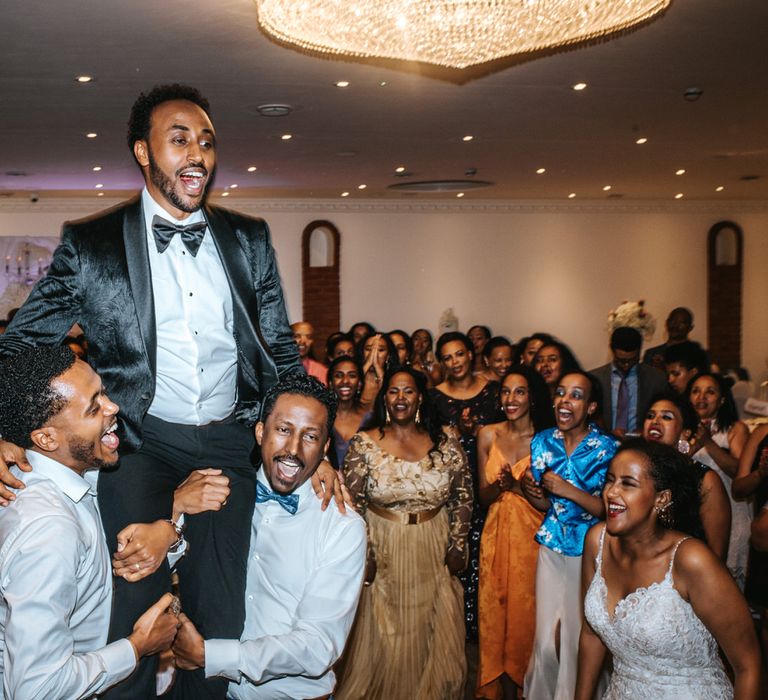 Wedding guests lifting the groom in a Jacquard tuxedo jacket on the dance floor 