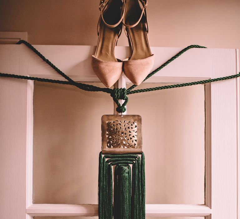 Brides shoes and green clutch bag hang over doorframe on the morning of her wedding day