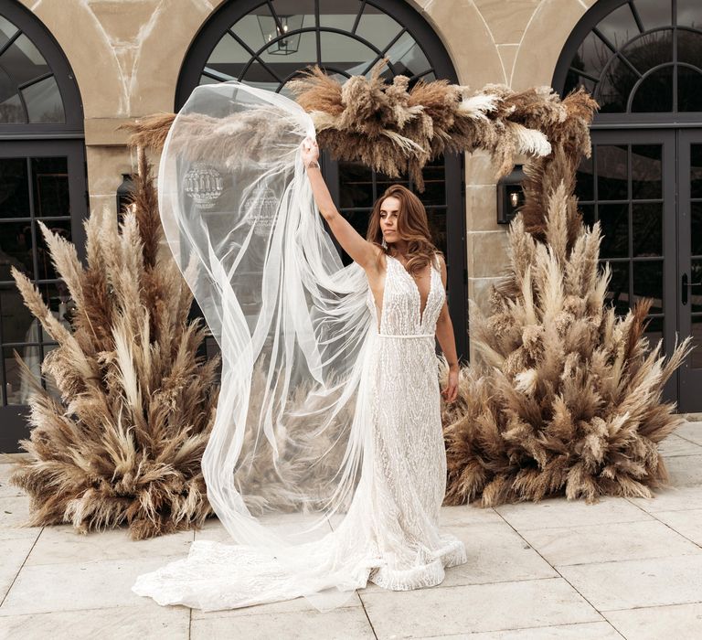 Bride in a lace wedding dress with sheer side panel waving her veil in the air 