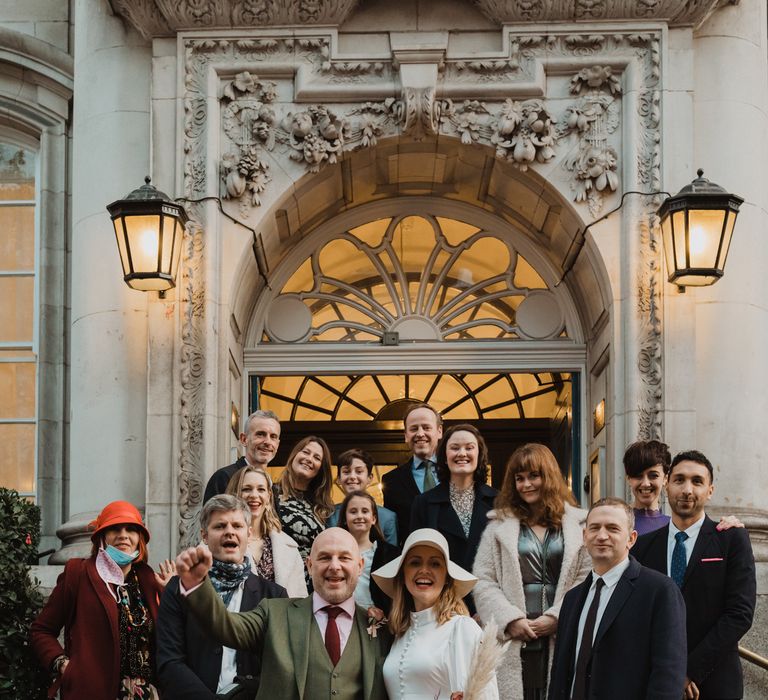 Bride & groom stand on the steps of Chelsea Town Hall with wedding party