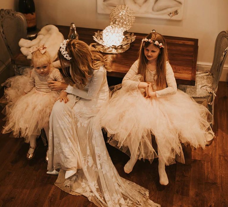 Bride in a long sleeve lace wedding dress sitting with her daughters in tutus at intimate wedding