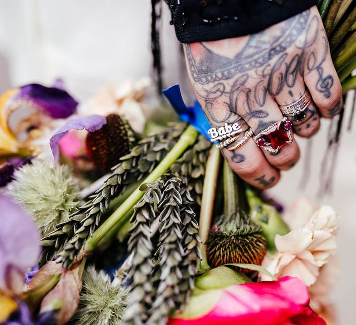 Bride with staking rings and hand tattoos holding her wedding bouquet 