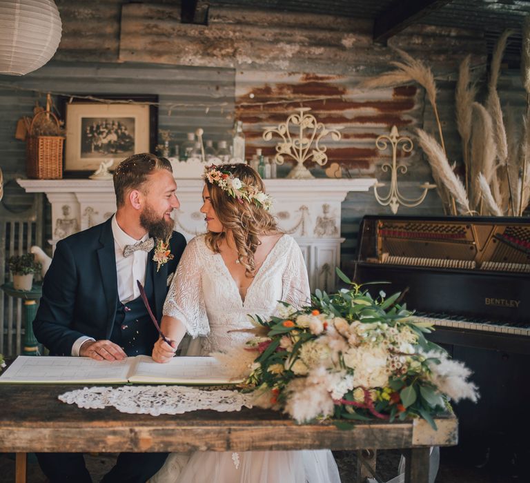 Bride & groom kiss one another as they sit and sign marriage certificate 