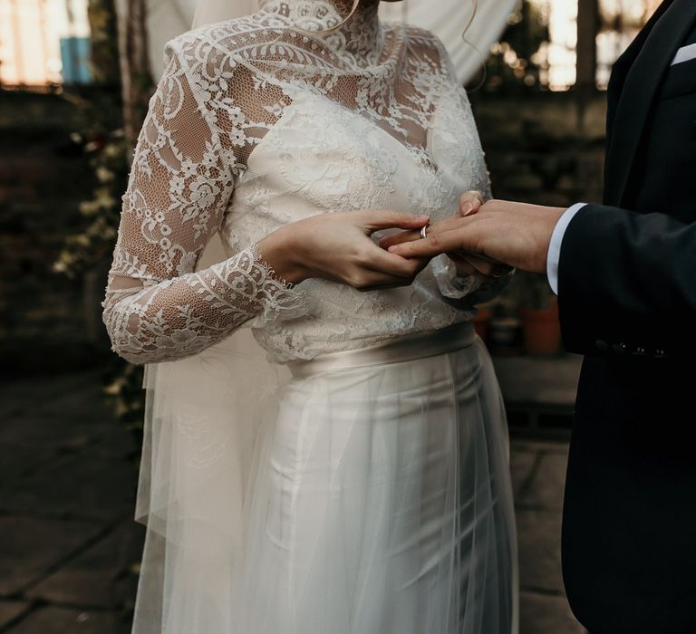 Bride in a long sleeve lace wedding dress putting on her grooms wedding band 