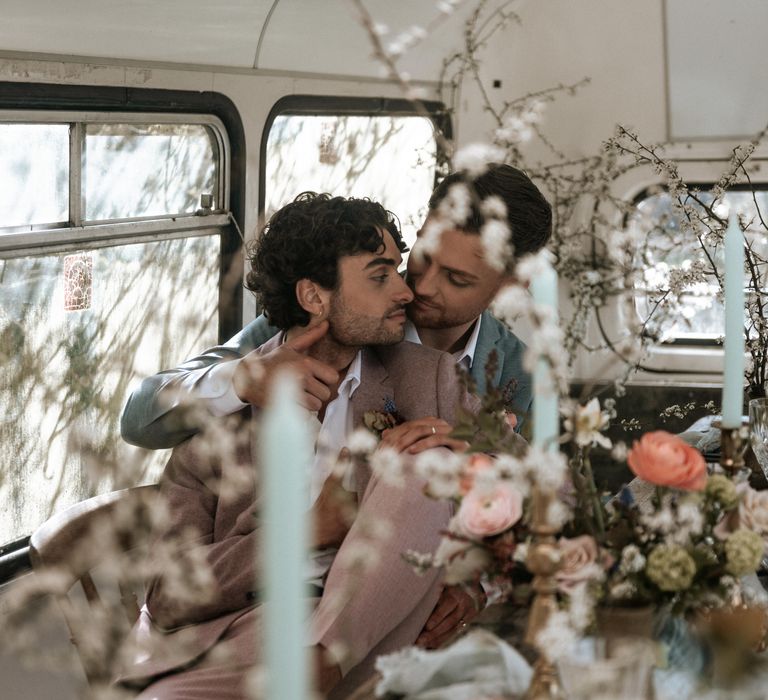 Grooms kiss one another in front of floral bouquets 