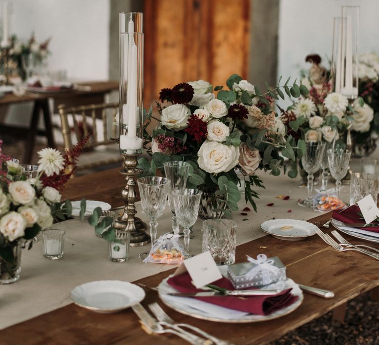 Rustic Italian table setting with accent deep red colour and large white candlesticks in front of wooden door