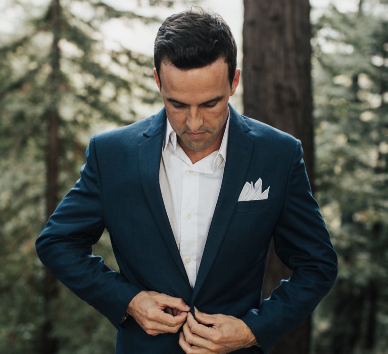 Groom does up blue suit on his wedding day outdoors in the forest