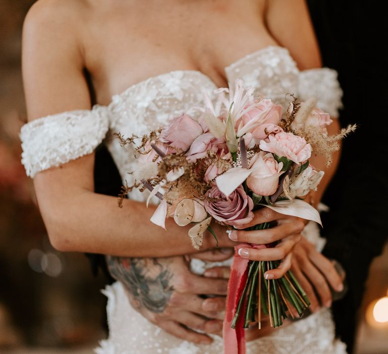 Bride with french manicured nails holding a small blush pink rose wedding bouquet tied with ribbon 