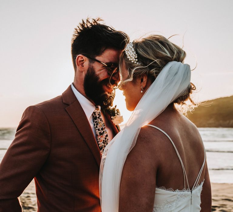 Bride & groom lean in to kiss one another on their wedding day as the sun sets behind them