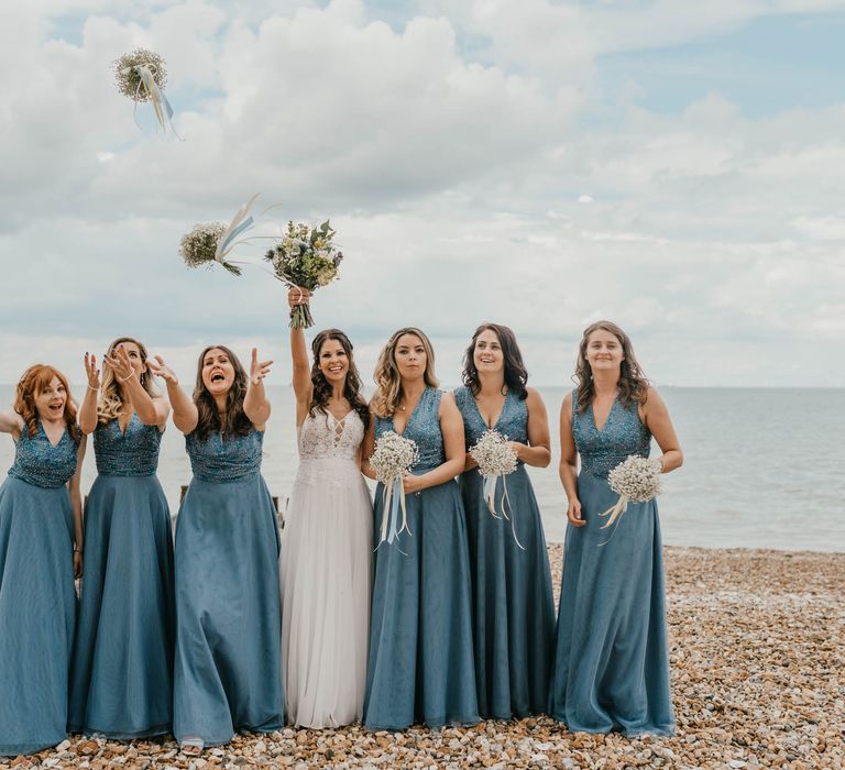 Bride and bridesmaids throw their bouquets in the air on the beach front