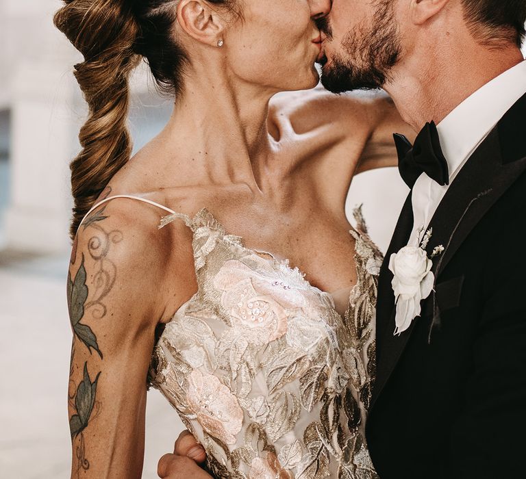 Tattooed bride in metallic styled boho chic gown kisses her groom on wedding day