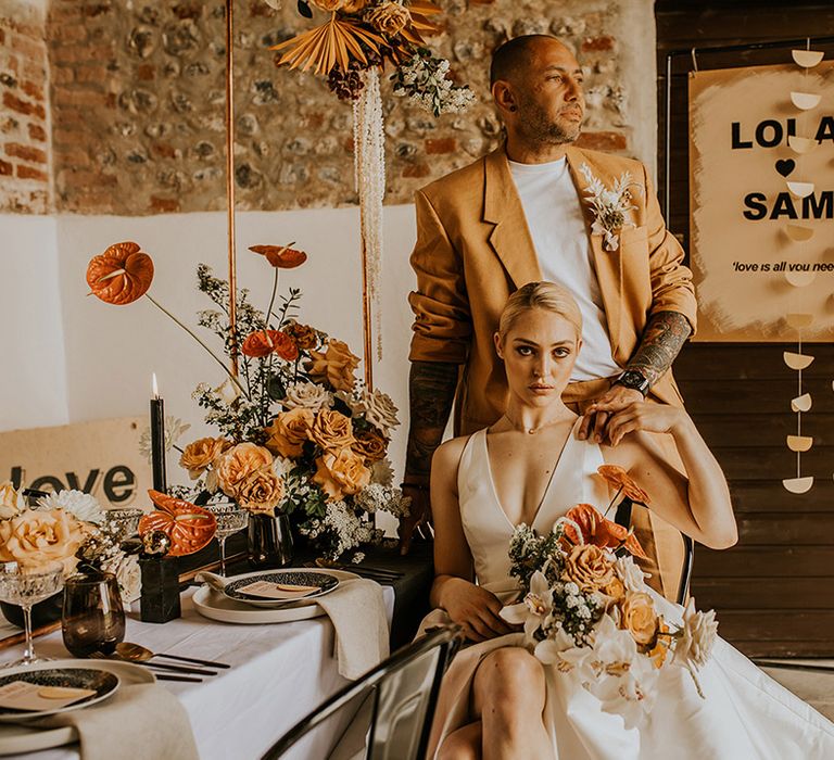 Contemporary orange and grey wedding reception decor with anthurium and rose floral arrangements, retro signs and a groom in a mustard suit 