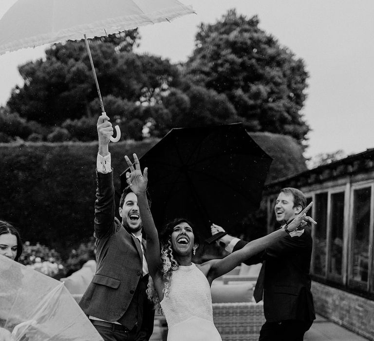 Bride celebrates as rain pours and umbrella is lifted above her head | Joshua Gooding Photography