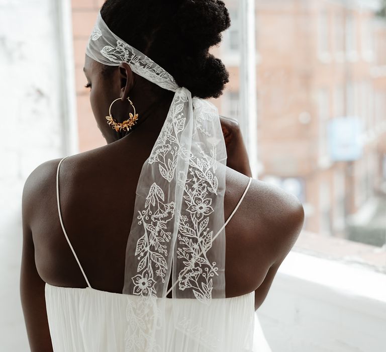 Black bride in a pleated wedding dress with thin straps wearing an embroidered bow wedding hair accessory 