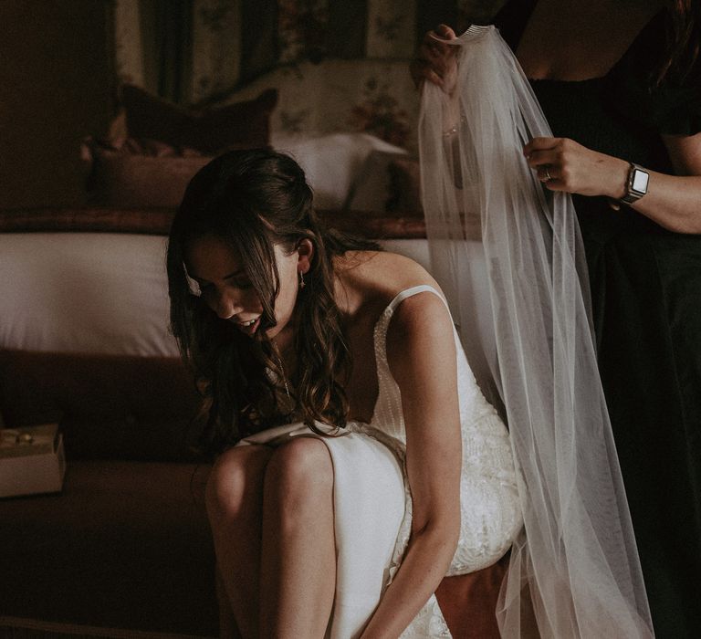 Bride ties her neutral shoes as her veil is slipped into her hair