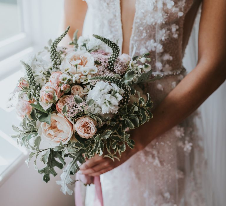 Bride in deep V Berta wedding dress with applique flowers holds white, blush pink and green bridal bouquet for summer wedding at Primrose Hill Farm