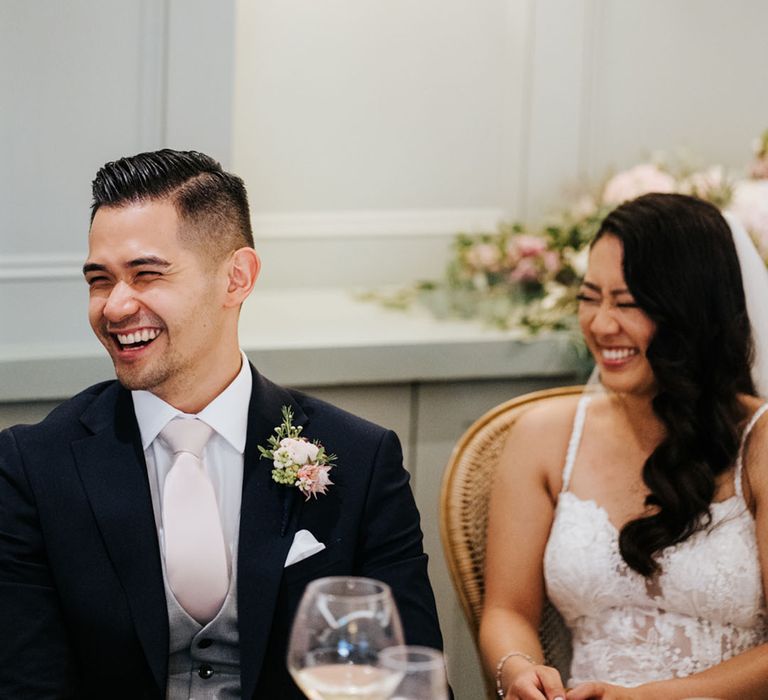 Groom in a navy suit with grey waistcoat and pale pink tie laughing during the Bingham Riverhouse wedding reception 