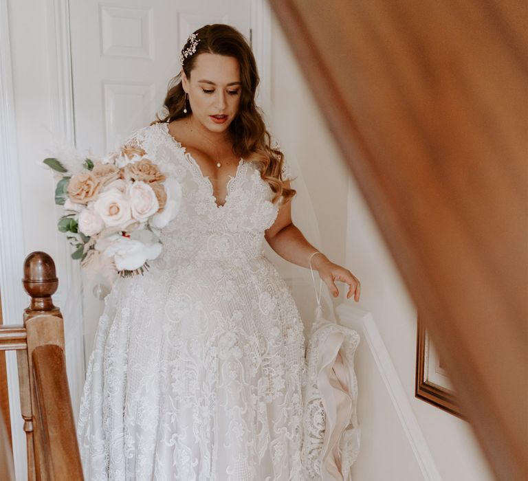 Bride in handmade wedding dress with mixed pink rose bridal bouquet walks down the stairs before DIY garden wedding in Bedfordshire