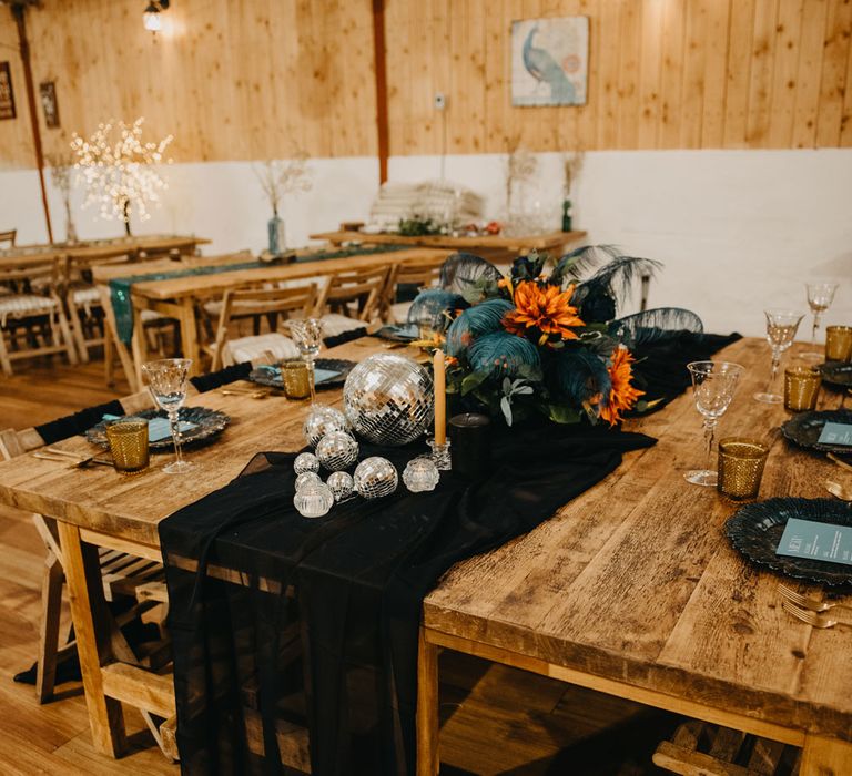 Wooden wedding table with black table runner, disco balls and orange and blue florals for rustic Wellbeing Farm wedding