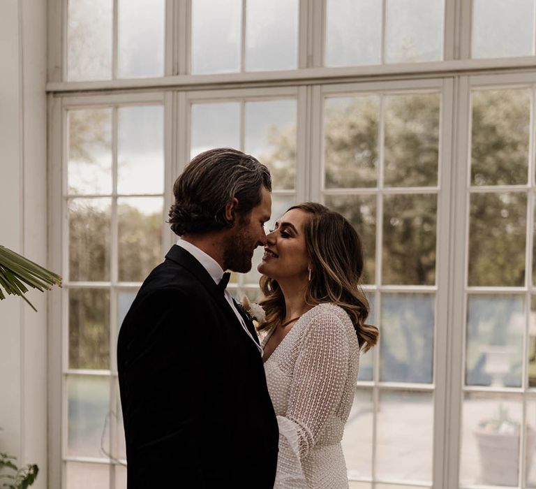 Groom in a tuxedo kissing his bride in a white beaded wedding dress with bell sleeves 