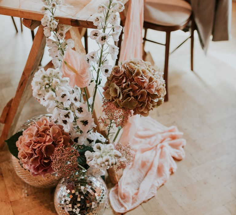 Pale pink floral bouquets complete with disco balls sit on the floor next to table