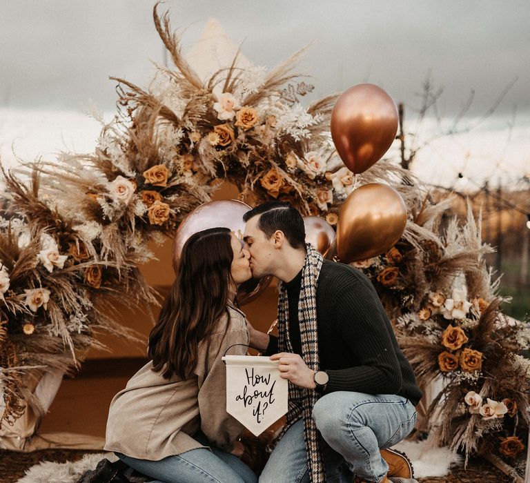 Bride and groom-to-be kissing after their boho campfire wedding proposal 