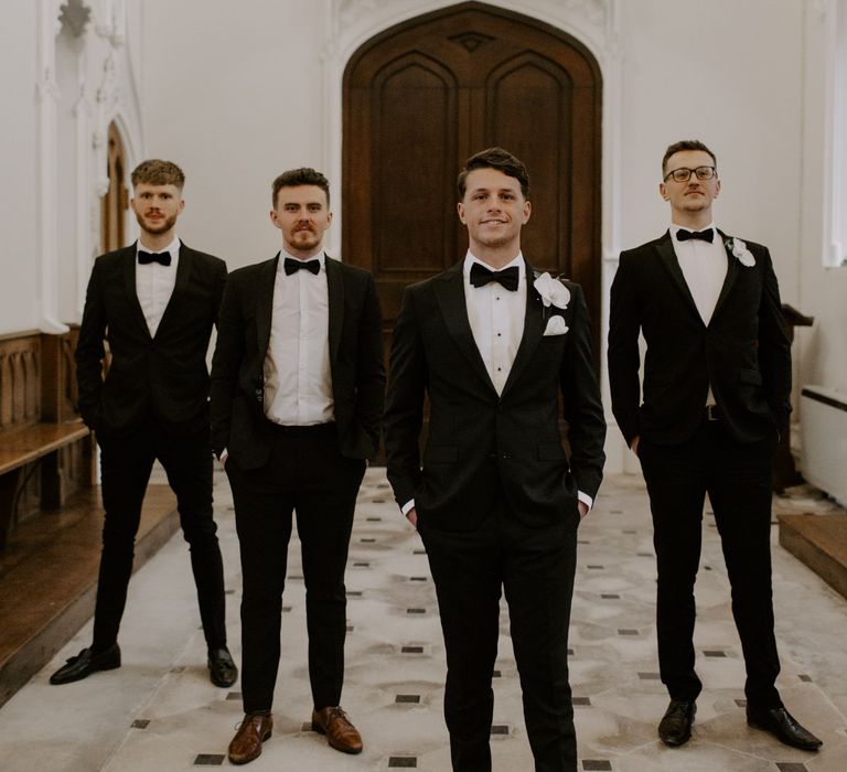 Groom stands with his groomsmen in black tie on wedding day 