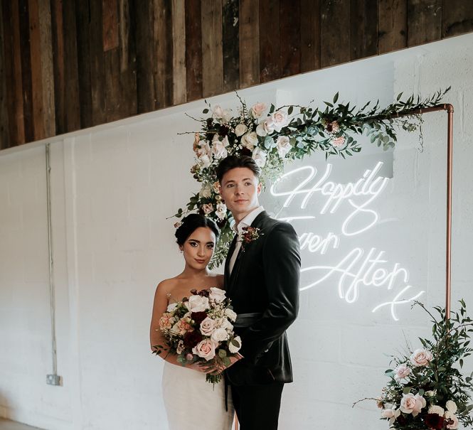 Bride & groom stand with one another in front of neon light