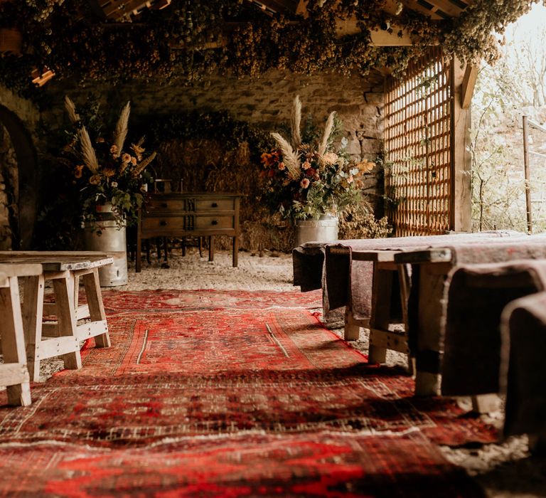 Boho rustic wedding aisle with red vintage rugs, wooden benches and floral installations for autumnal wedding