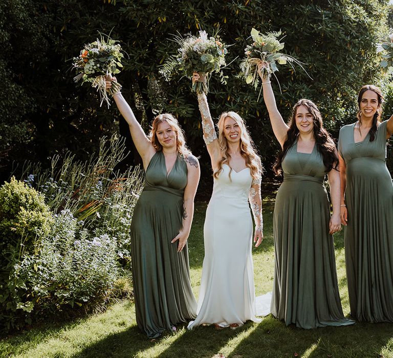 Bride stands with bridesmaids as they lift their bouquets in the air 