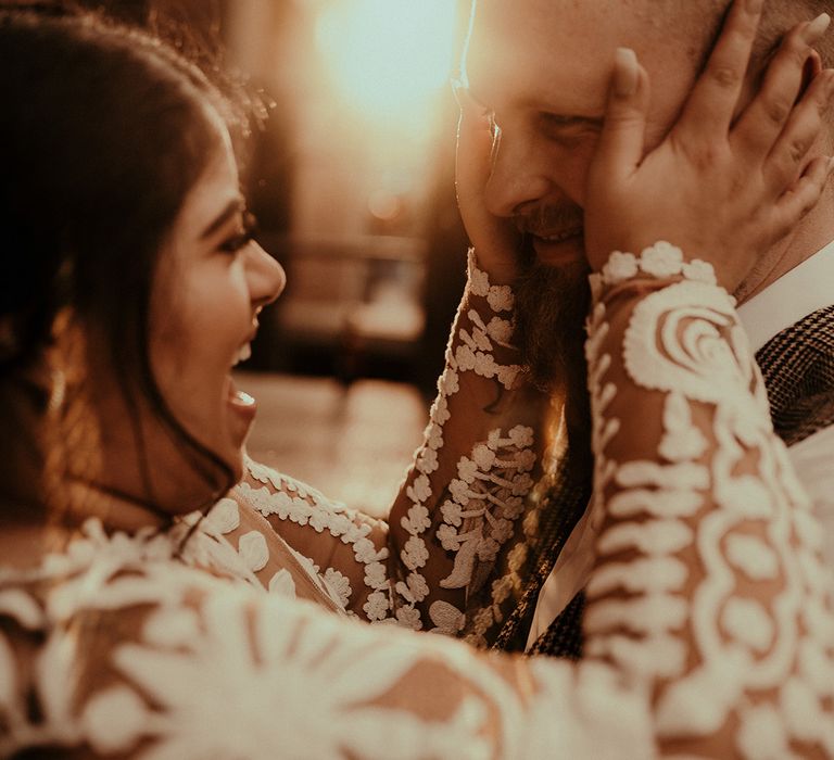 Indian bride in a long sleeve lace wedding dress and manicured nails embracing her grooms face 