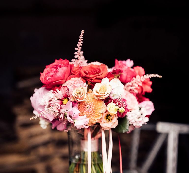 Red, pink and white mixed wedding bouquet in glass vase with ribbon detailing 