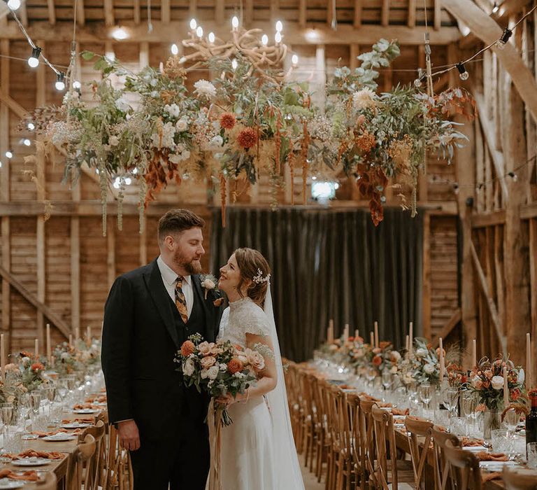 Bride and groom under flower installation at rustic wedding at The Barns at Redcoats