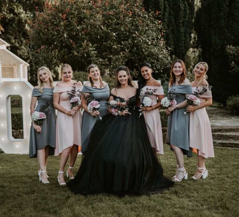 Bride wears black gown and stands with her bridesmaids who wear pink and green pastel bridesmaid gowns