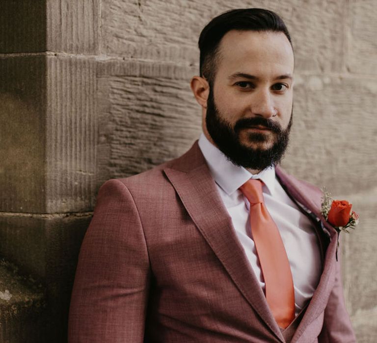 Bearded groom in a dusky pink wedding suit with orange tie