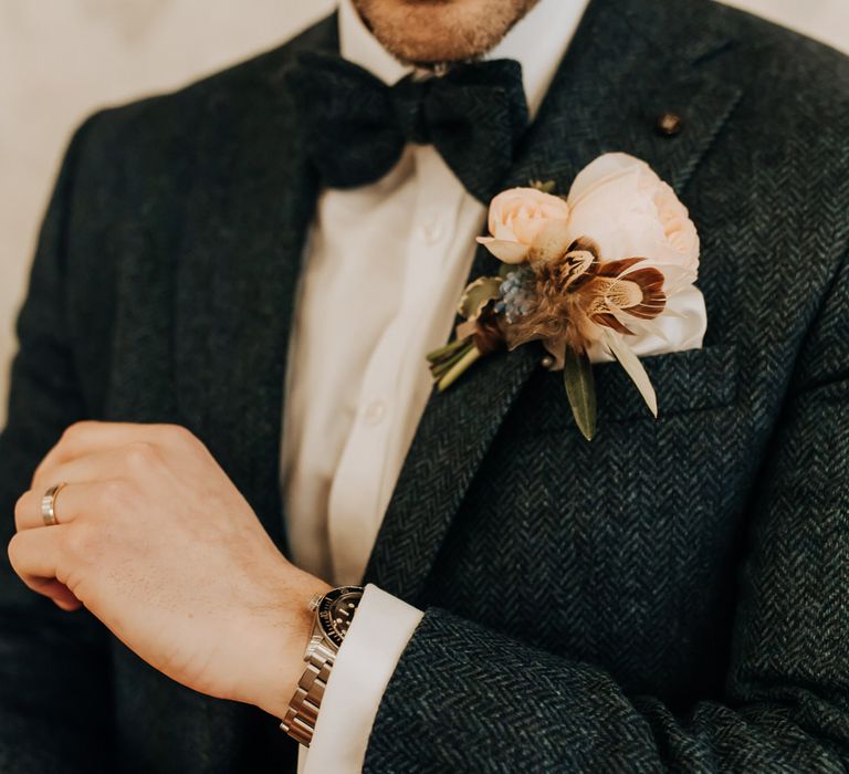 Groom in navy tweed three piece suit with bow tie and rose buttonhole adjusts his cuffs