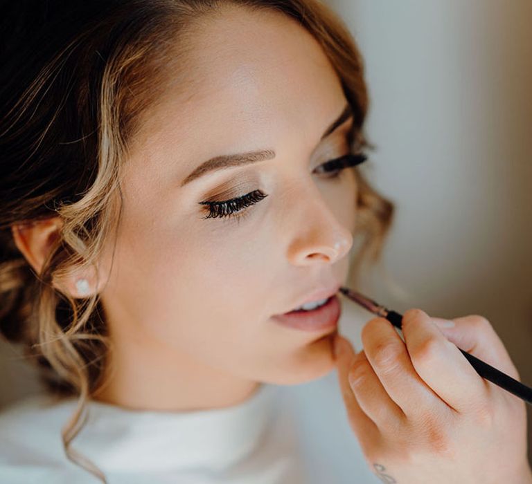 Bride on her wedding morning having her wedding day makeup applied with natural eyeshadow, winged eyeliner and barely there lipstick.