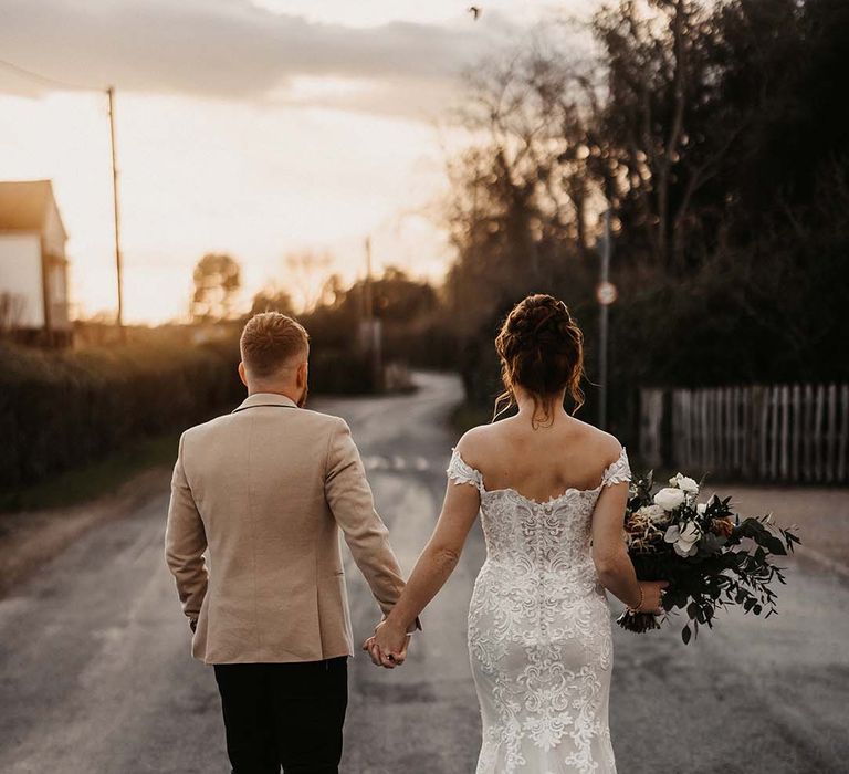 Bride in off the shoulder lace wedding dress with button details and mermaid style with groom in beige suit jacket 