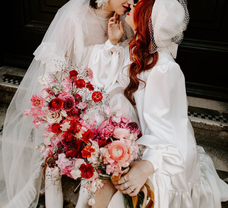 Bride with red wavy hair in a long sleeve wedding dress kissing her bride in a high neck wedding dress with long veil 