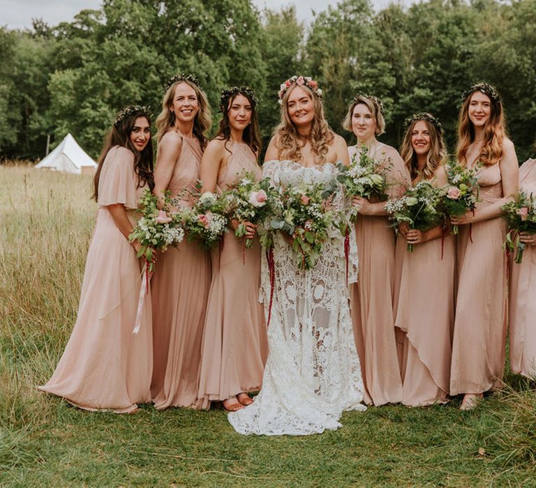 Bride in off the shoulder medieval wedding dress with custom sleeves stands with seven bridesmaids in pink dresses with rose bouquets