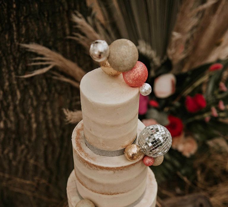 Three tier semi naked wedding cake with ball and disco ball wedding decor at festival themed wedding 