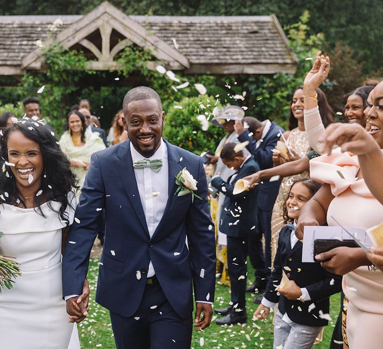 Bride and groom exit their Sudanese wedding ceremony to a confetti exit with groom in blue suit and mint green bow tie